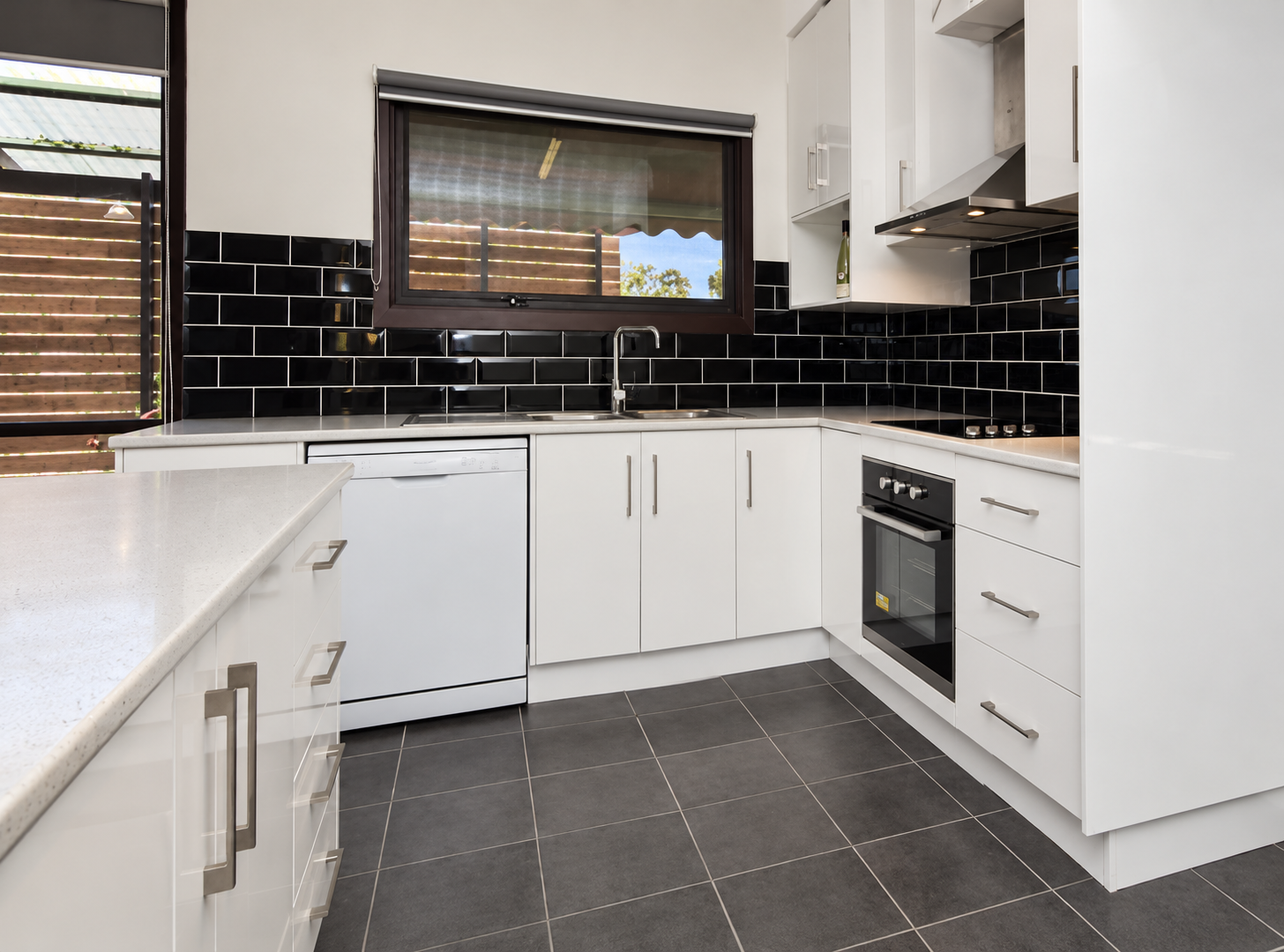 Renovated kitchen with white cabinets, dark tiled splashback and stone benchtops after renovation
