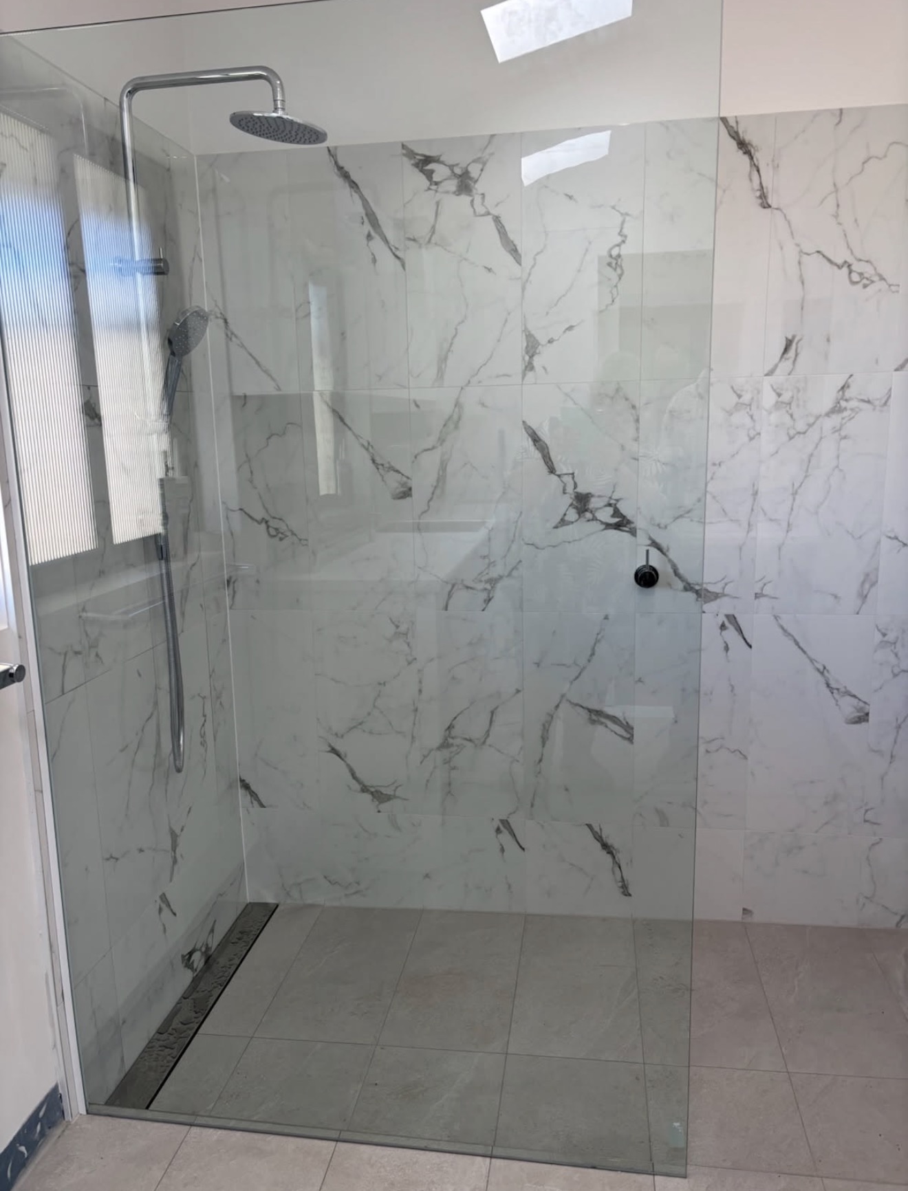 Bathroom after renovation with a frameless walk-in shower and marble-look wall tiles