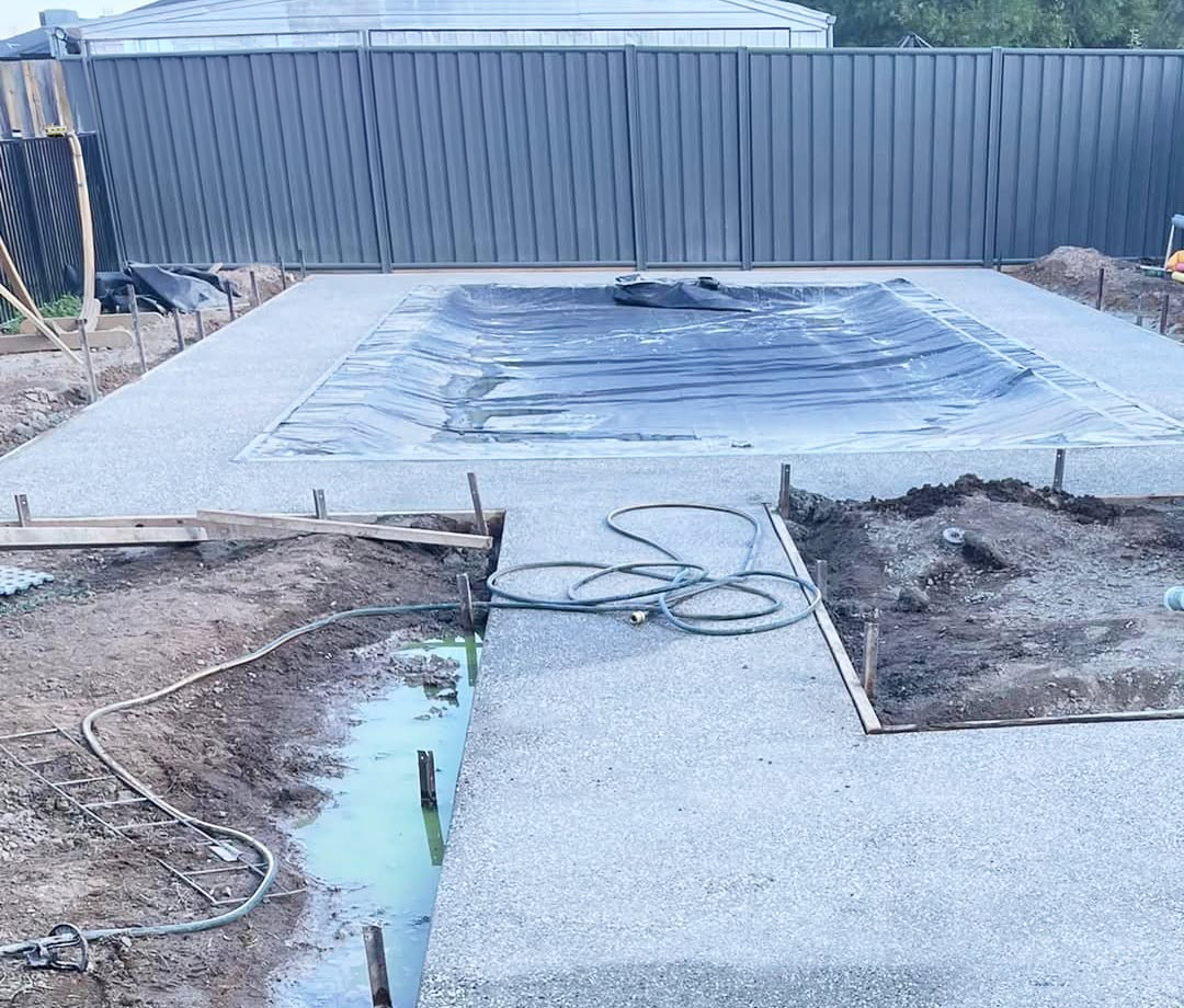 Pool area with unfinished paving and bare garden beds before landscaping